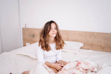 The girl is in bed in the morning, rejoices at waking up with a good mood.Portrait pretty young girl on bed in modern apartment in the morning. She keeps eyes closed and looks satisfiedの写真素材
