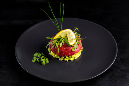 Beef tartar with egg served on a black stone plate. Tartar on a black plate with avocado, herbs, salt and chicken yolk. Raw tartare meat.Black background. Top view.の写真素材