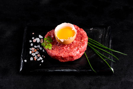 Beef tartar with egg served on a black stone plate. Tartar on a black plate with herbs, salt and chicken yolk. Raw tartare meat.Black background. Top view.の写真素材