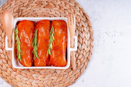 Fresh chicken meat on a light background, copy space. Raw marinated chicken fillet in a baking dish with serving plates.の写真素材