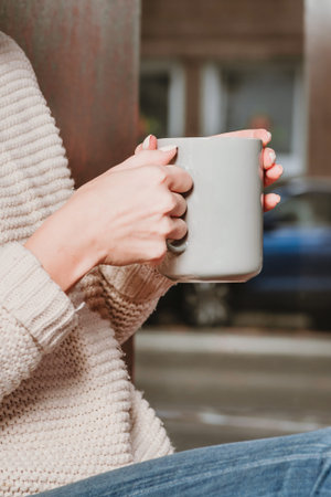 A girl in a beige sweater holds a cup of tea in her hands.