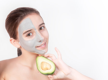 Portrait of a young attractive girl with a cosmetic mask on her face. Close-up. Face skin care concept.Beautiful girl with a cosmetic mask made of clay on her face. Cosmetic procedures.の写真素材