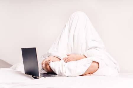 Distance work.Efficient Young Millennial Girl Sitting on a Bed in the Morning, Uses Laptop Computer. In the early morning, the girl works at the computer in bed and does not want to work.の写真素材