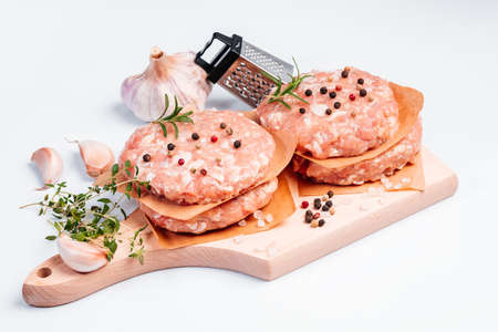Raw chicken burger on a white plate in a rosemary branch and spices. Instant meat. Grilled hamburgers.Raw Hamburger, meatballs on white background.Fast food at home.Convenience food, precooked.の写真素材