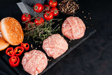 Grilled hamburgers.Copy space.Raw chicken burger on a kitchen board with a rosemary branch, tomatoes, garlic, paprika and spices. Instant meat.の写真素材