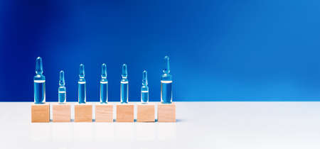 Glass ampoules close up. Ampoules with medicine on wooden blocks on a blue background, place for text.Pharmaceutical laboratory.Copy space.Health concept.Medical ampoules on a blue background.の写真素材