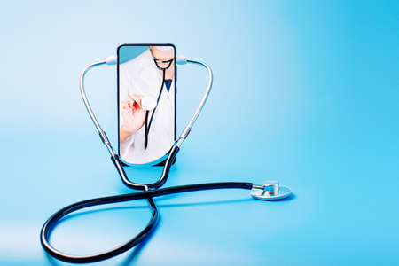 Female doctor chatting online with patients.Copy space. Stethoscope on a blue background with place for text, online doctor. Calling a doctor by phone.Health concept. The doctor can examine the patient via video call.の写真素材