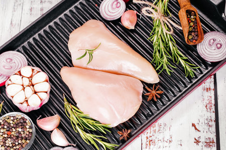 Chicken fillet in a skillet with spices and vegetables on a dark background. Raw chicken meat cut...