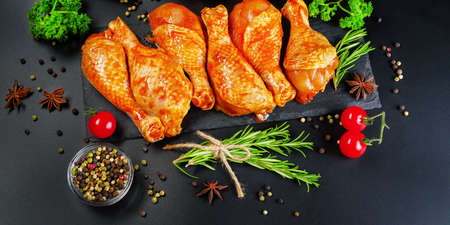 Barbeque marinated chicken dramsticks on a black cooking board on a black background with fresh rosemary leaves. Semi-finished product, Marinated product, cooking.Background banner of meat with spices.の写真素材