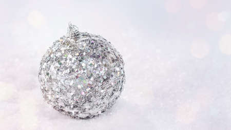 Shiny, silver glass Christmas ball on snow on a light background. Glittering,Shiny background.Christmas, winter, new year concept.copy space.Winter Background.Xmas and New Year holiday, bokeh, lightの写真素材