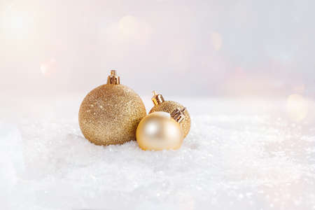 A variety of golden shiny Christmas balls on the snow on a light background.の写真素材