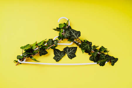 Hangers entwined with plants on yellow background with copy space.Conscious and environmentally friendly consupmtion in shopping.Zero waste.Shopping,sale,promo, concept.Top view flat lay copy spaceの写真素材