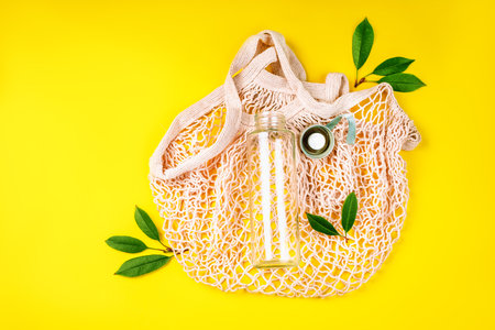 The concept zero waste.Life without Plastic.Reusable glass bottle for water on yellow background.May bottle.Cotton bag,glass bottle and bamboo tubes.Lets go shopping.Ecological, natural materials.の写真素材