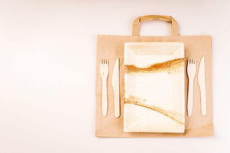 Disposable eco cutlery,plates,spoons,knives,forks on a light background.Craft paper bag for food...