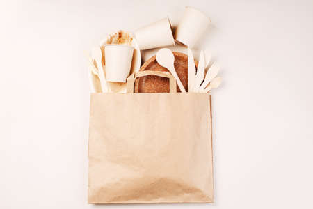Disposable eco cutlery,plates,spoons,knives,forks on a light background.Craft paper bag for food delivery.Copy space.Eco craft paper tableware,cups,fast food containers.Recycling,eco-friendly concept.の写真素材