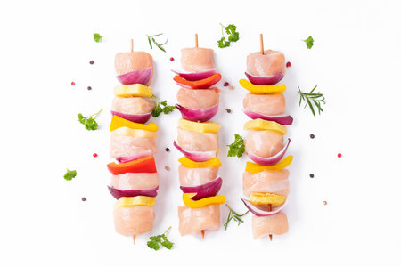 Skewers with pieces of raw meat, red, yellow and green pepper.Raw pieces of chicken skewers with pepper onion and pineapple on a white background.Uncooked mixed meat skewer with peppers.Top view.の写真素材