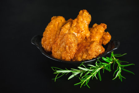 Chicken wings fried until half cooked, semi-finished product.Semi-finished chicken wings on a dark background with fresh herbs. Half-finished. Quick cooking at home. Fast food. Breaded chicken wings.の写真素材