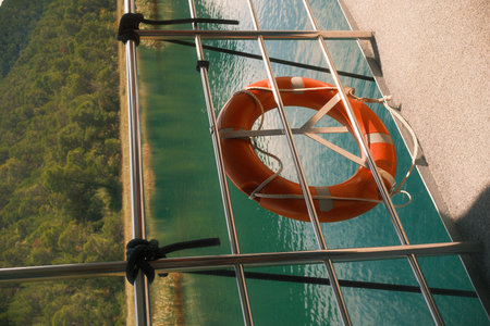 Orange lifebuoy on boat railing over turquoise water and forestの写真素材
