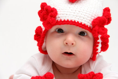 Little baby with knitted white hat with red flowers