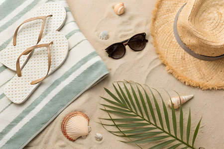 Beach accessories on sand. Flip flops, hat, sunglasses, seashells and palm leafの素材
