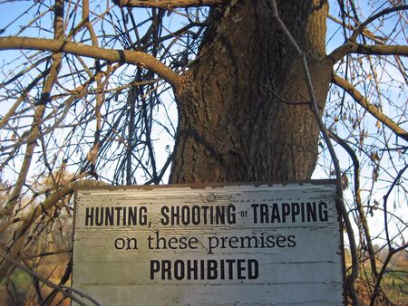 White wooden sign prohibiting hunting, shooting, and trapping posted on a tree in rural Vermontの写真素材