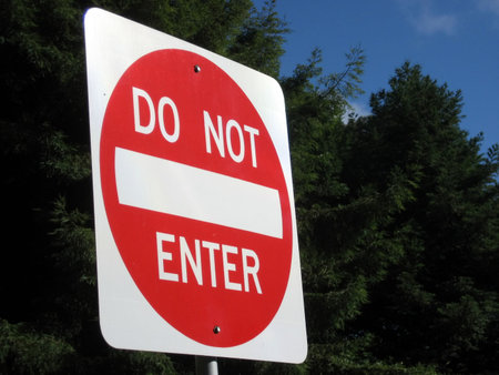 Bright red and white Do Not Enter Sign against a background of green trees and blue sky