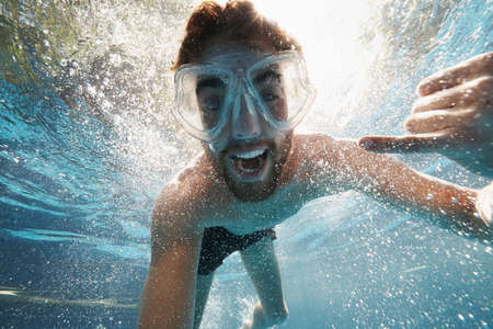 Underwater shot of a young man wearing swimming goggles in a poolの写真素材