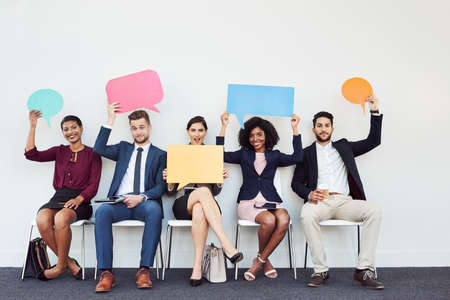 Studio portrait of a group of young businesspeople holding speech bubbles while sitting in a row against a white backgroundの写真素材