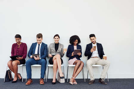 Studio shot of a group of young businesspeople using wireless technology while sitting in line against a white backgroundの写真素材