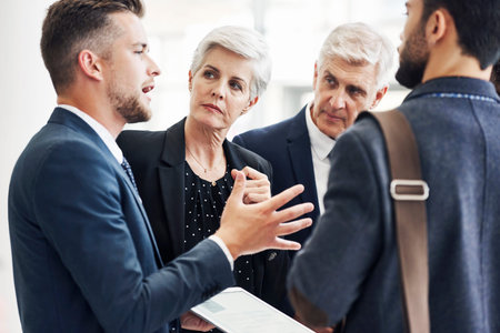 Cropped shot of a diverse group of businesspeople standing and using a tablet while talking in the...