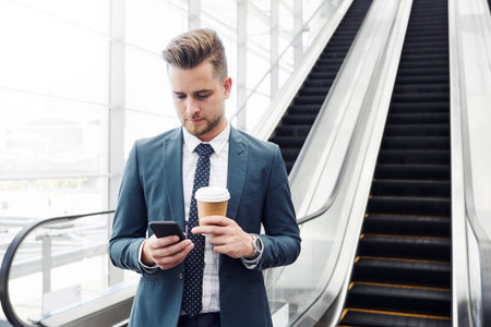 Cropped shot of a handsome young businessman using a smartphone while standing alone in the...