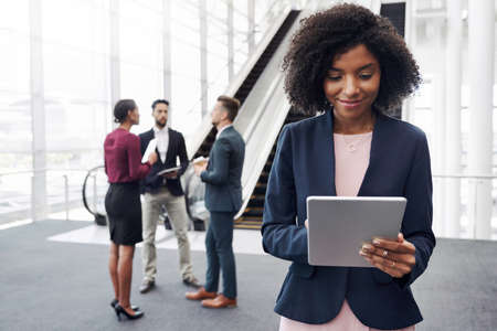 Cropped shot of an attractive young businesswoman using a digital tablet in an office with her colleagues standing in the backgroundの写真素材