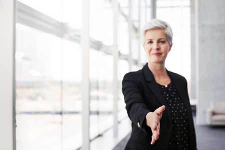 Portrait of a confident mature businesswoman extending her arm for a handshake in a convention centerの写真素材