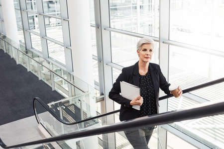 Shot of a mature businesswoman traveling on an escalator in an airportの写真素材