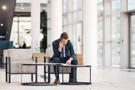 Full length shot of a handsome young businessman sitting and talking on his cellphone while in the officeの写真素材