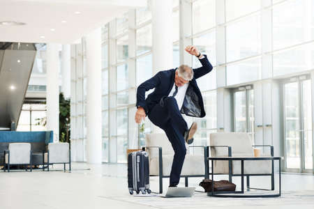 Full length shot of a mature businessman feeling stressed and stepping on his laptop aggressively while in the officeの写真素材