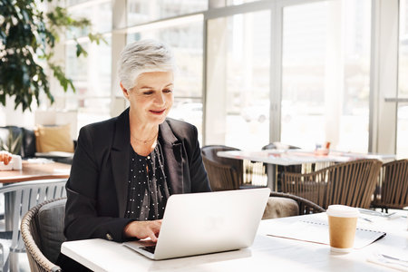 Shot of a mature businesswoman using a laptop while sitting in an airport cafeの写真素材