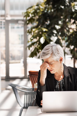 Shot of a stressed out mature businesswoman using a laptop while sitting in an airport cafeの写真素材