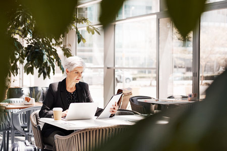 Shot of a mature businesswoman using a laptop while sitting in an airport cafeの写真素材