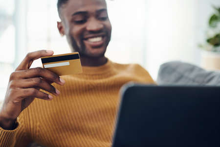 Shot of a young man using a laptop and credit card at homeの写真素材