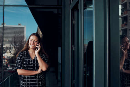 Shot of a young businesswoman talking on a cellphone while standing on the balcony of an officeの写真素材