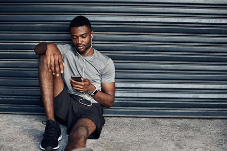 Shot of a sporty young man wearing earphones while using a cellphone against a grey backgroundの写真素材