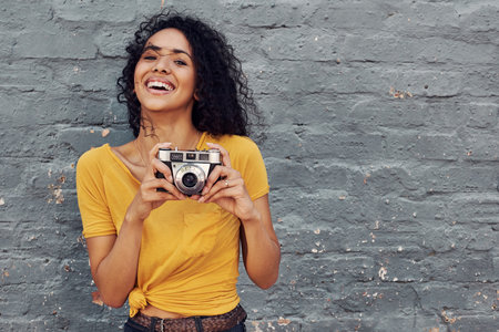 Cropped portrait of an attractive young woman holding a camera and standing alone against a gray backgroundの写真素材