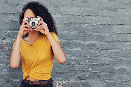 Cropped shot of an attractive young woman holding a camera and taking a picture while standing against a gray backgroundの写真素材