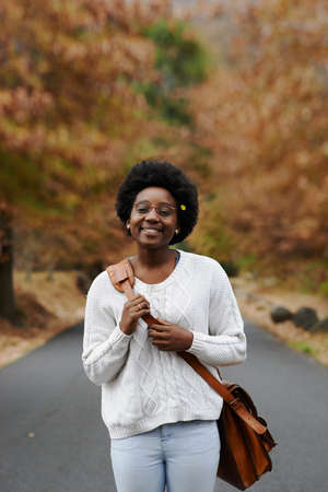 A young woman walking along a road on an autumn dayの写真素材