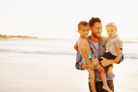 Shot of a young man and his adorable sons having fun at the beachの写真素材