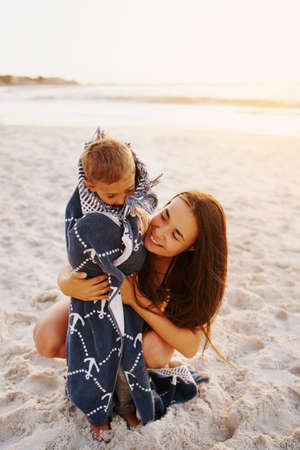 Shot of a mother lovingly wrapping her son in a towel at the beachの写真素材