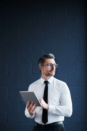 Cropped shot of a mature corporate businessman working on a digital tablet against a dark backgroundの写真素材