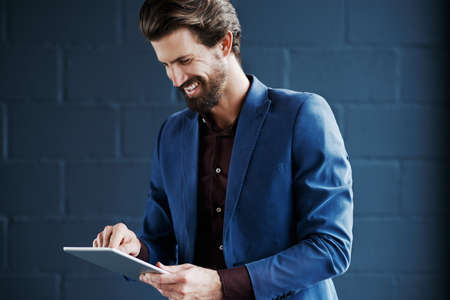 Cropped shot of a young corporate businessman working on a digital tablet against a dark backgroundの写真素材