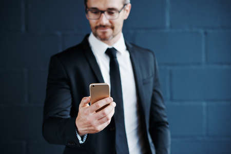 Cropped shot of a mature corporate businessman texting on his cellphone against a dark backgroundの写真素材